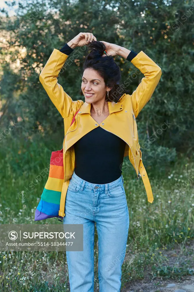 Woman posing with a handbag on her shoulder. She smiles and is outdoors.
