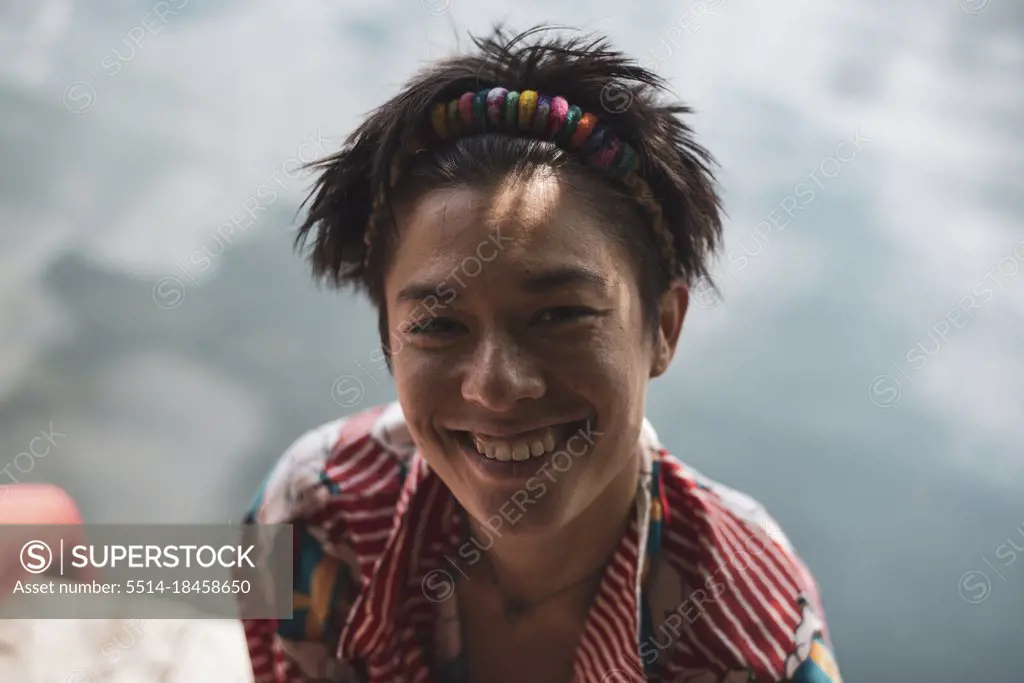 non-binary asian person smiles in colourful shirt by lake
