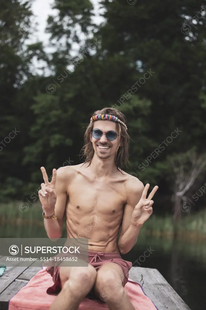 Smiling fit queer young man sitting by lake at festival in Poland