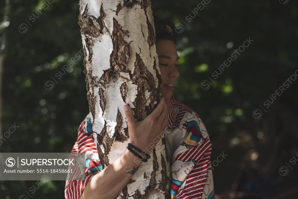 Non-binary person in colourful shirt hugging a birch tree in summer