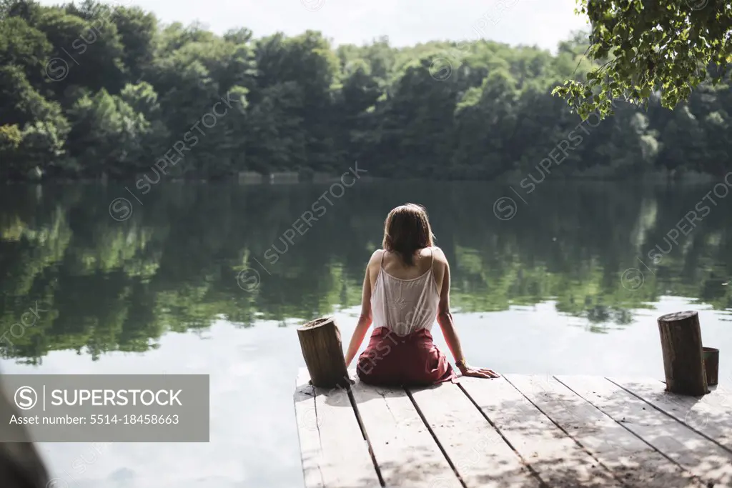 Solitary person sitting on wooden jetty looking at lake in summer