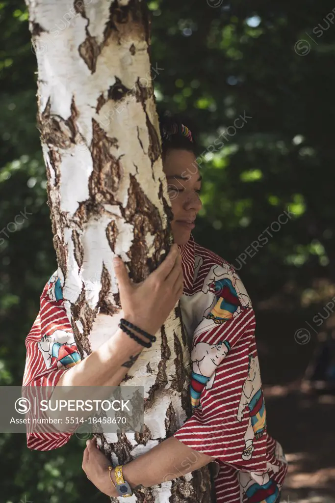 Mixed race non-binary person hugging birch tree in forrest