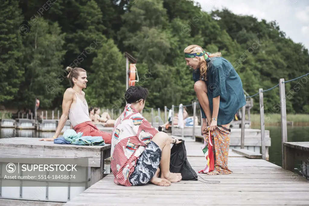Queer friends enjoying summer sun and swimming on wooden jetty by lake
