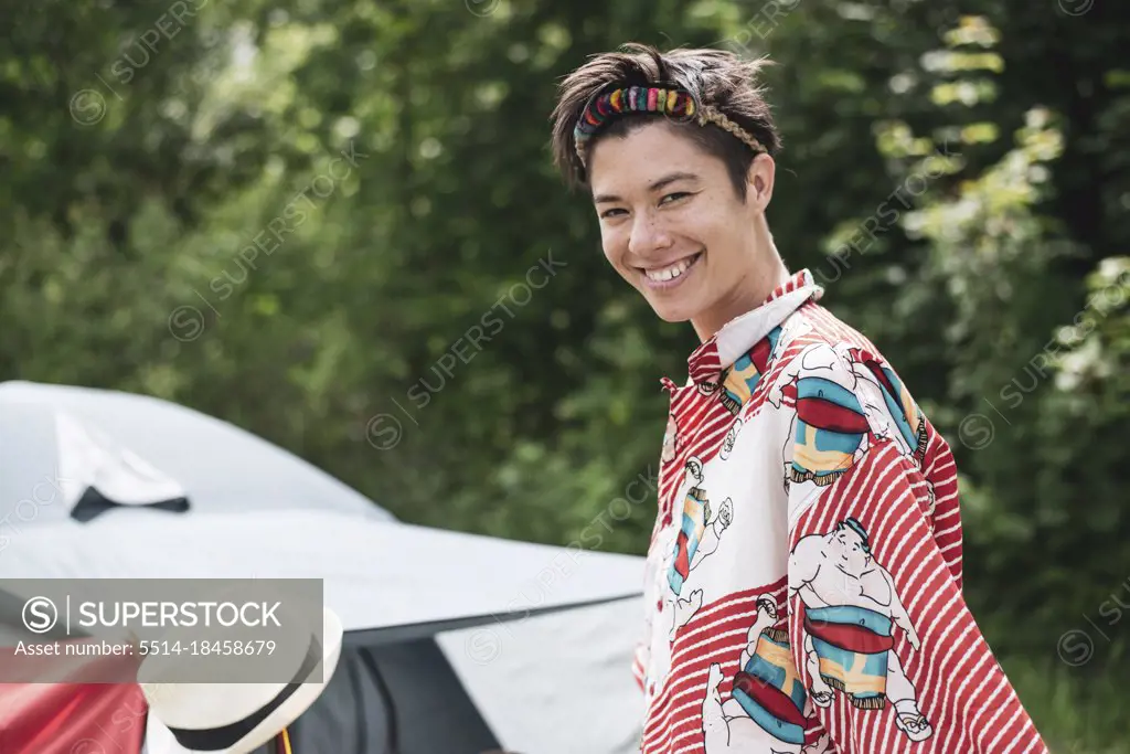Smiling queer mixed-race woman colourful shirt, headpiece in campsite