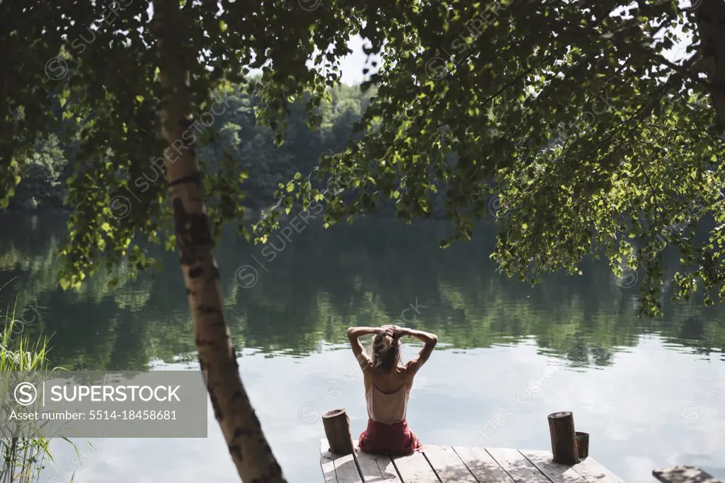 Young person relaxing lakeside on wooden jetty under trees in summer
