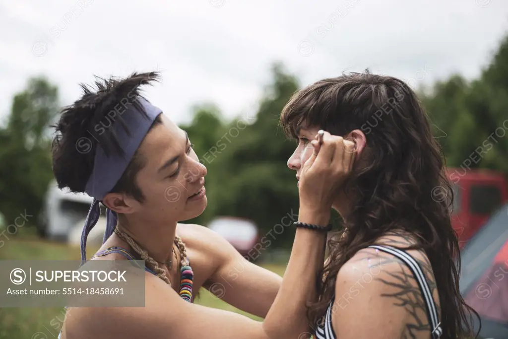 non-binary asian face paints woman with curly hair at festival camp