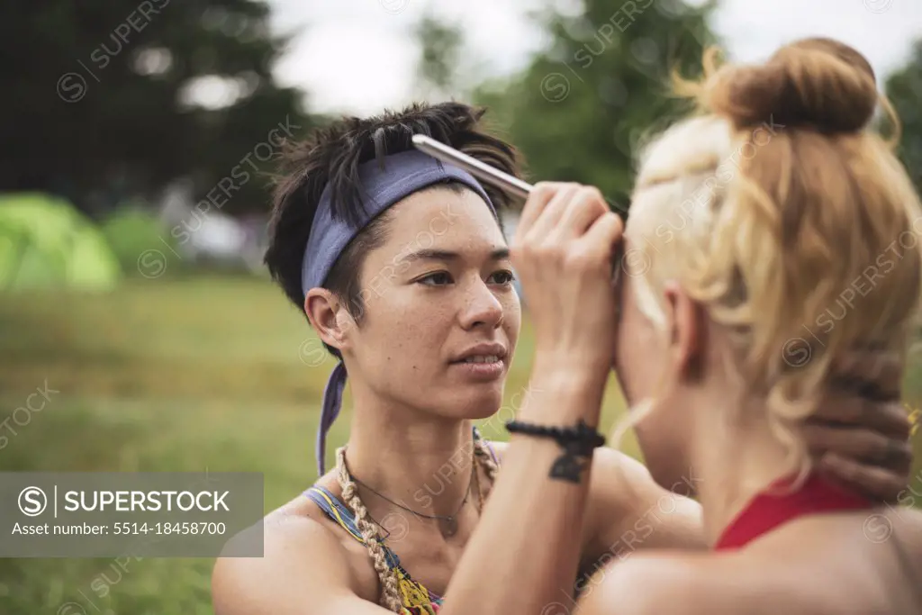 mixed-race athletic woman paints friends face camping at festival