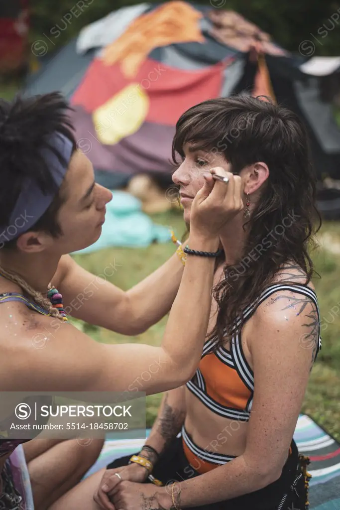 two fit healthy queer women paint face and glitter body at camp