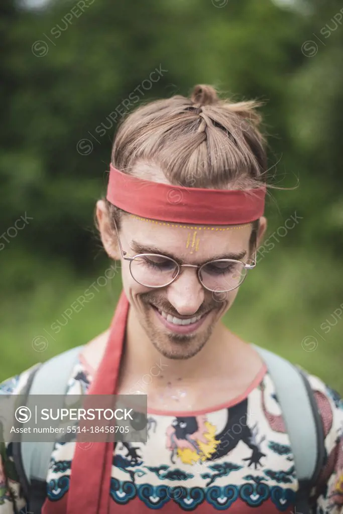 Colourful queer man with glasses smiles  facepaint in nature