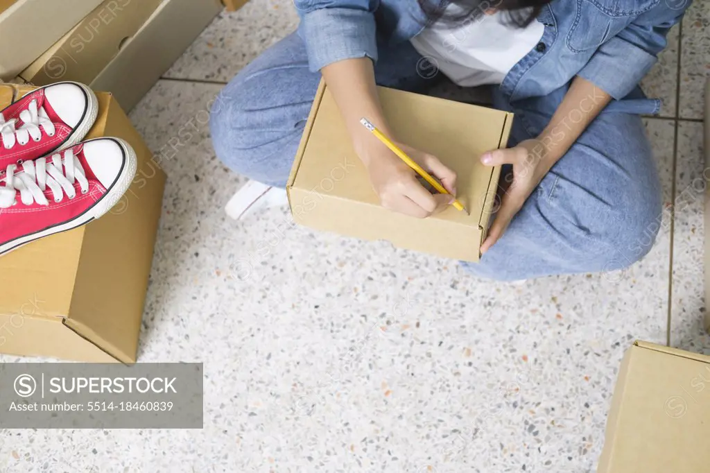 Online small business owner writing address on parcel box.