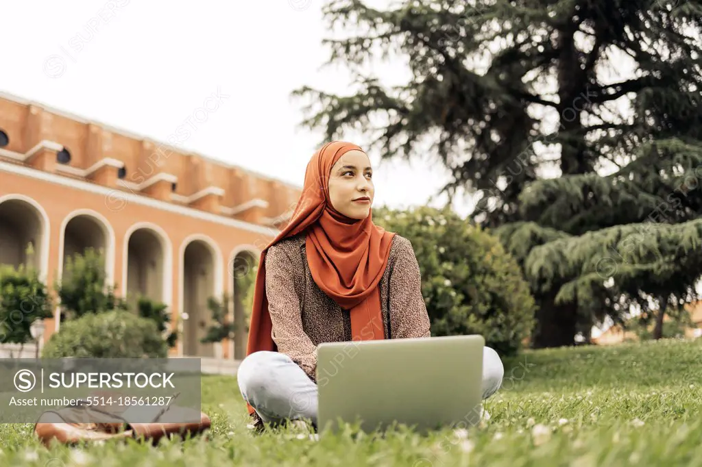 Muslim woman siting on the grass using a computer