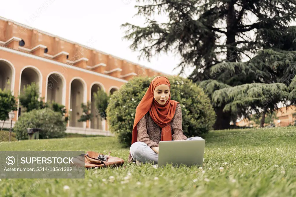 Muslim woman siting on the grass using a computer