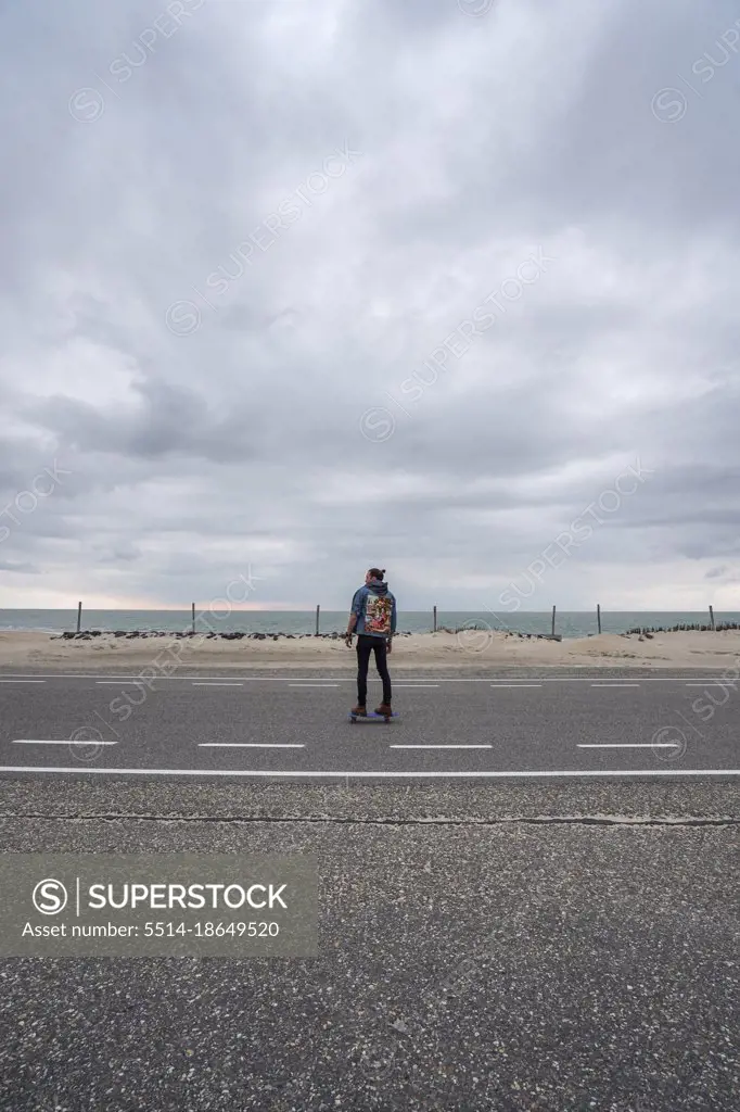 A man with long hair skating on a empty road in europe