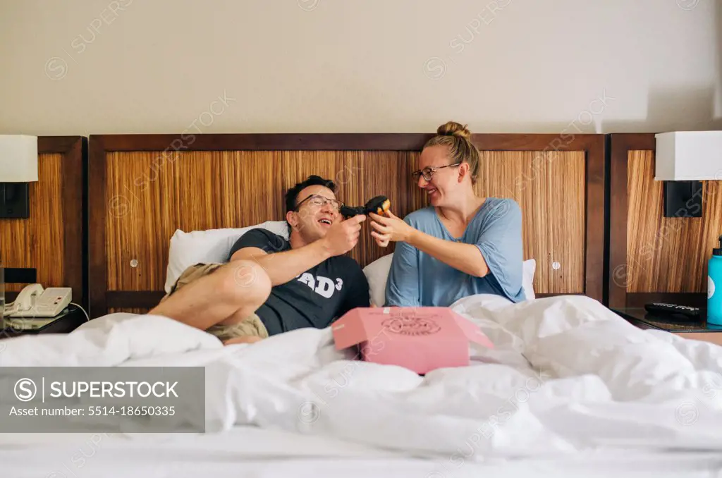 Parents eating donuts in bed while enjoying staycation at hotel
