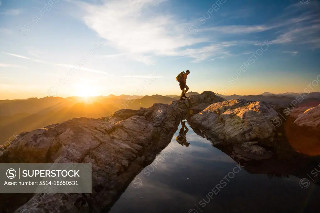 Backpacker hiking over rocky mountain terrain at sunset.
