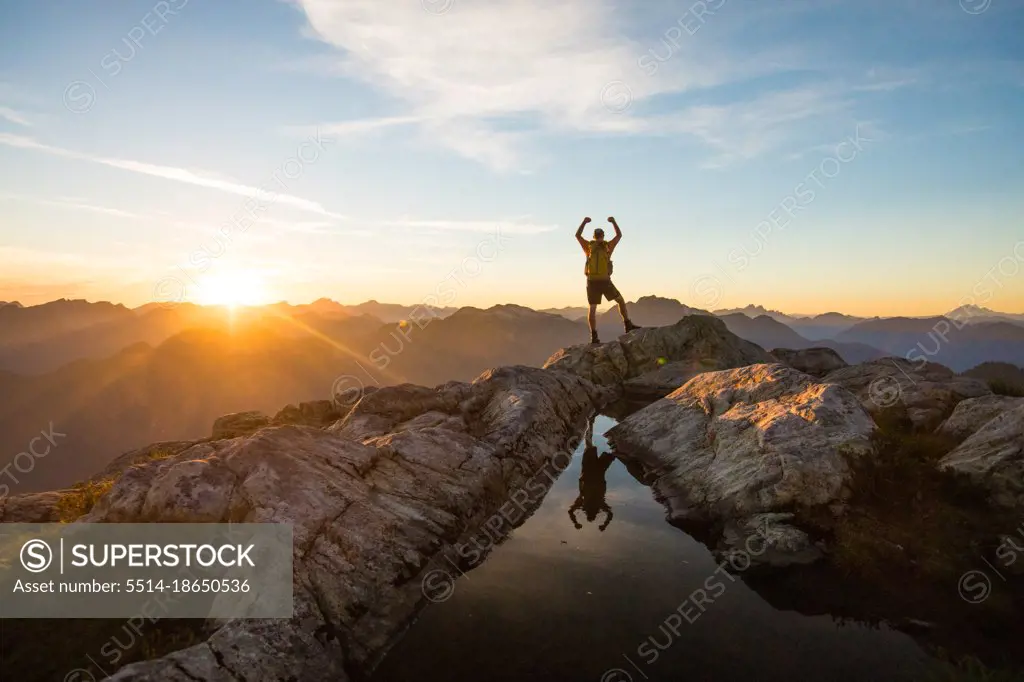 Successful hiker reaches mountain summit at sunset.
