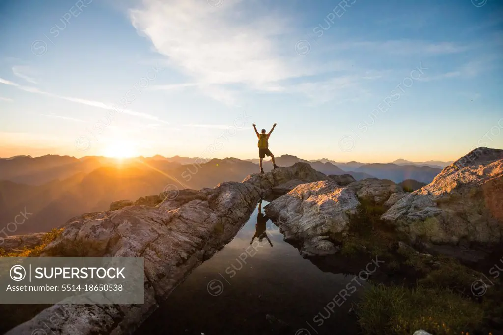 Hiker standing on summit, reaching for the sky, success.