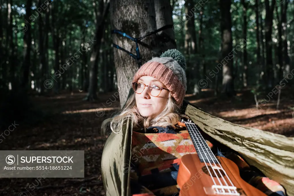 woman sat on a hammock in a forest with a ukulele in autumn
