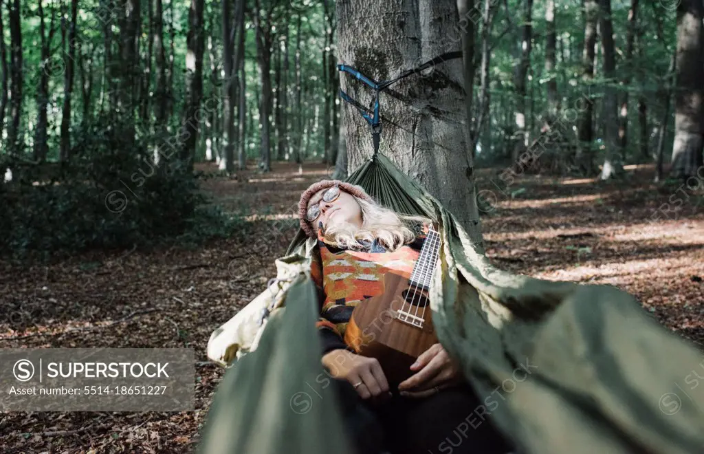 woman sleeping in a hammock with her ukulele in the forest