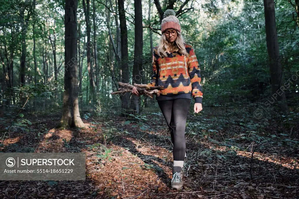 woman walking in a forest with sticks fire collecting