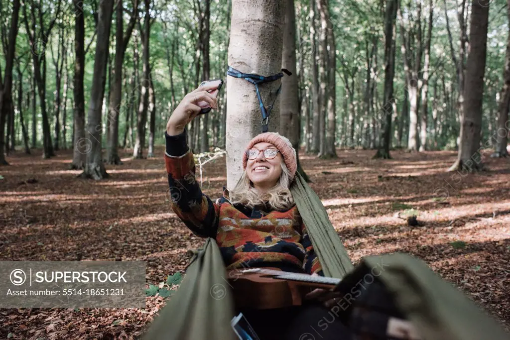 woman sat in a hammock in the forest taking a selfie