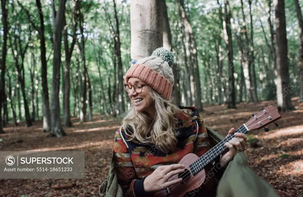woman happily sat in a hammock playing the ukulele in a forest