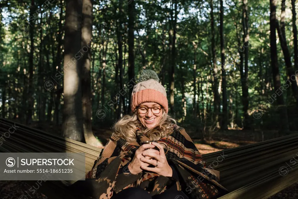 woman sat happily in a hammock in the forest having coffee