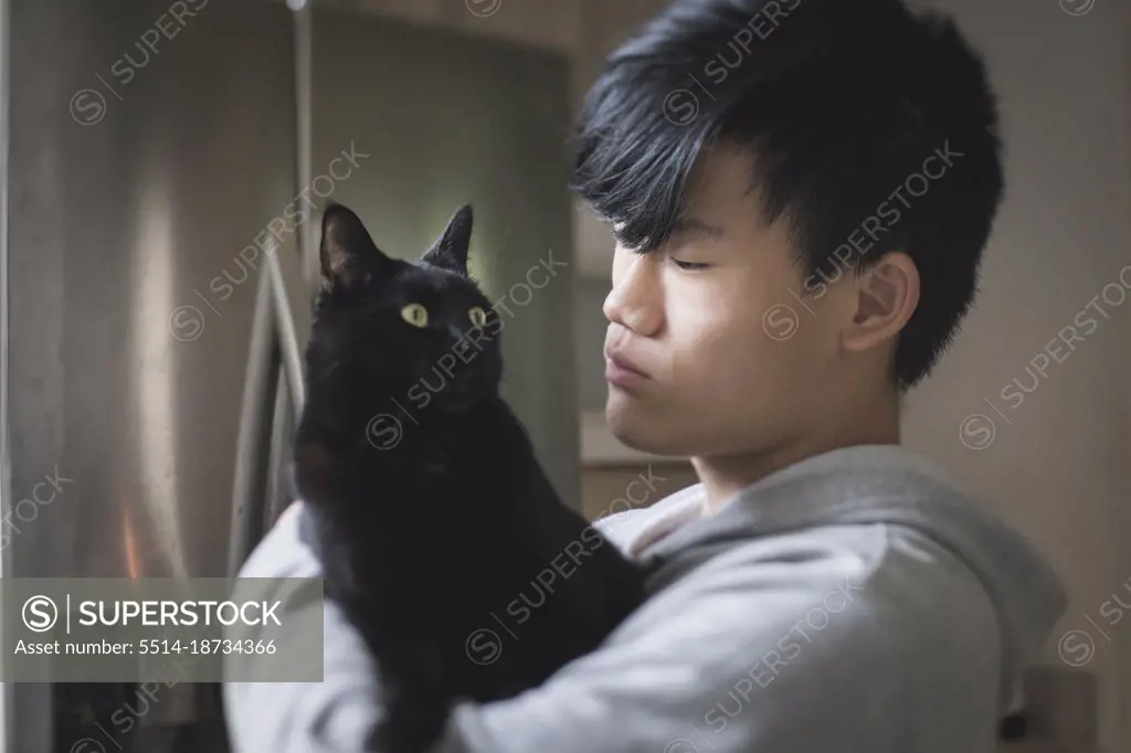 Asian teen boy in hoodie holds black cat