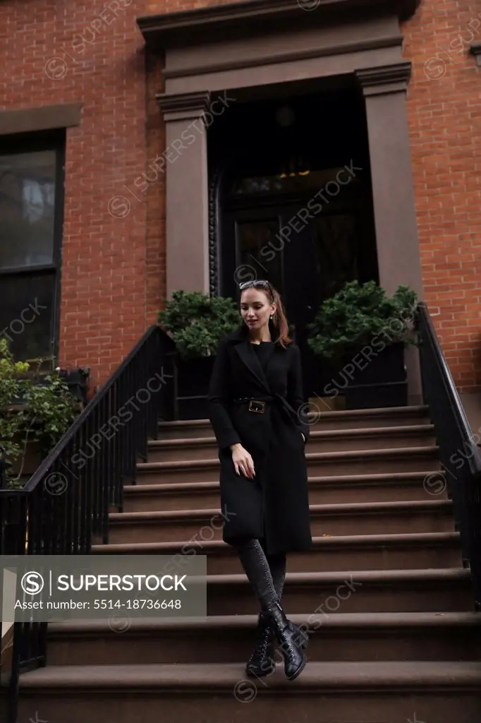 Young woman in black coat stand on the steps of the house