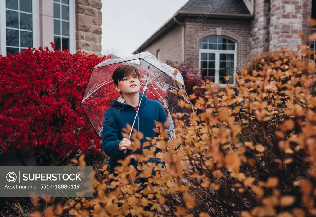 Boy holding umbrella in front of house on a rainy fall day.
