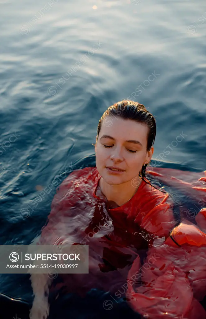 woman in wet red dress with closed eyes in blue water