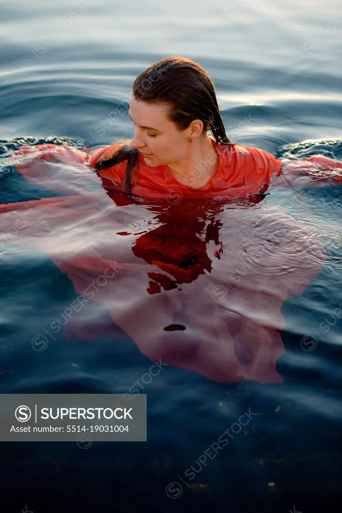 a woman in a wet red dress with wet hair swims in blue water