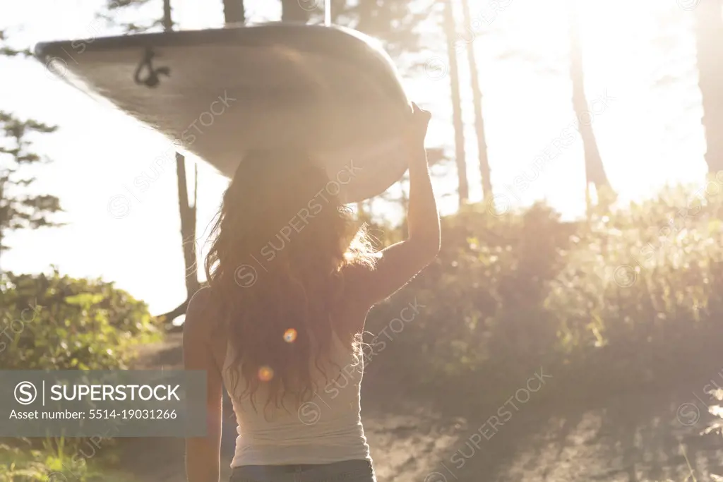 Woman carrying surfboard down trail to the ocean