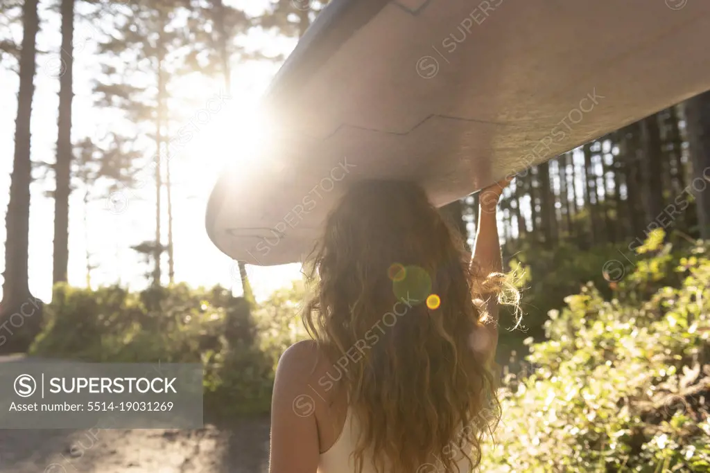Woman carrying surfboard on her head down trail to the ocean