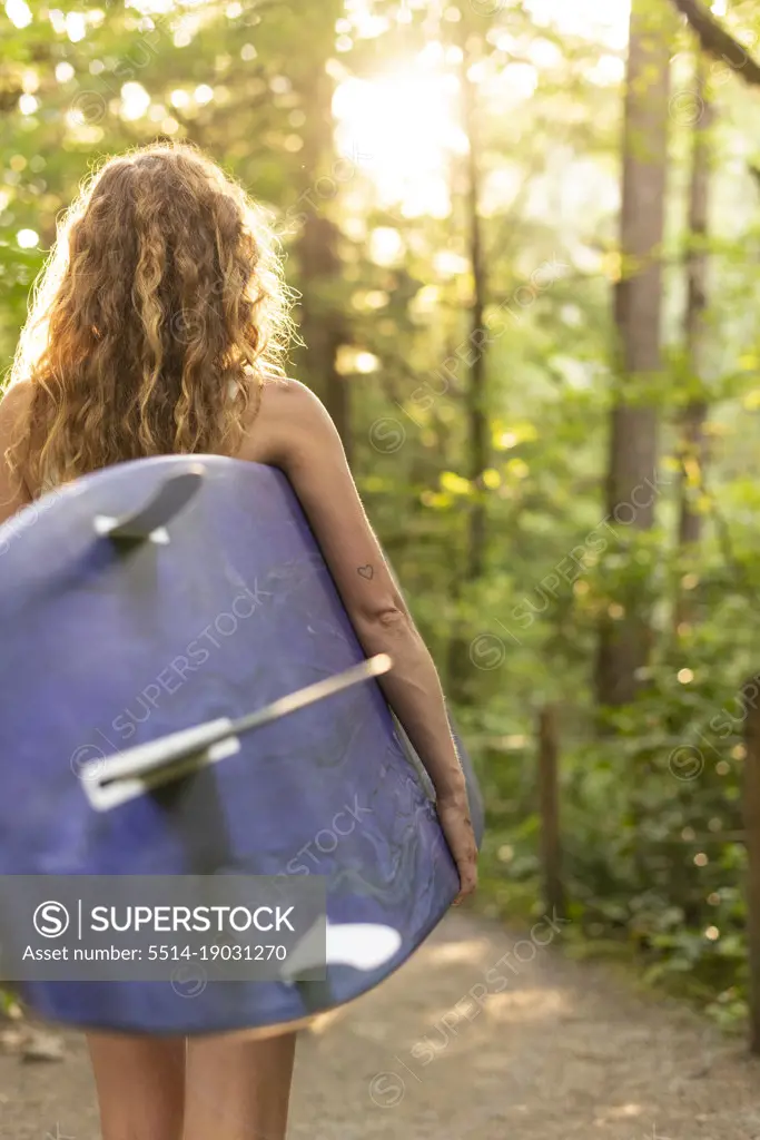 Woman with heart tattoo carrying a surfboard down trail to beach