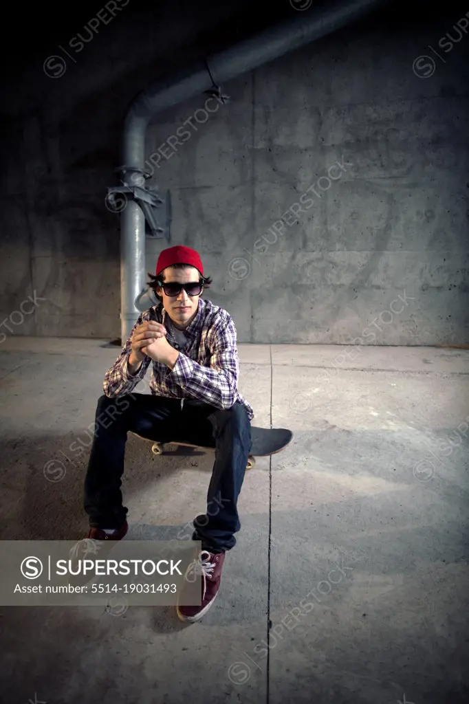 Skateboarder sitting on board under overpass