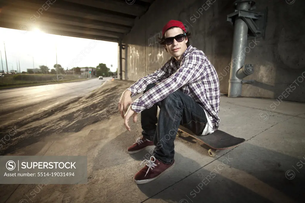 Skateboarder sitting on board under overpass