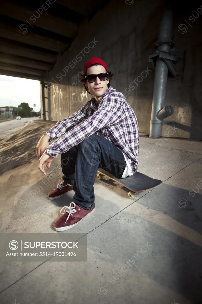 Skateboarder under overpass sitting with sunglasses