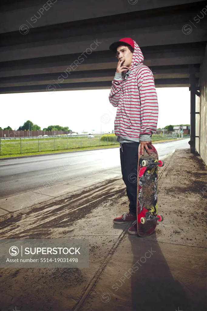 Skateboarder under overpass standing with board