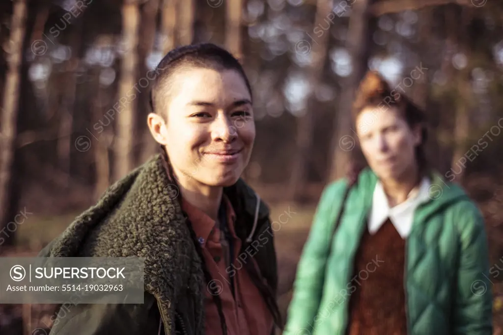 Mixed race person with shave smiles at camera with friend in woods