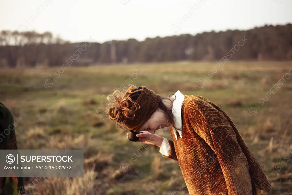 Female in earthy brown colours laughs drinking tea outside in field