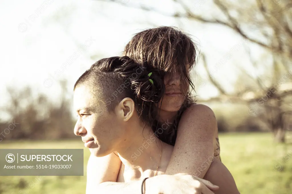 Queer female couple embrace in sunny afternoon on grass meadow