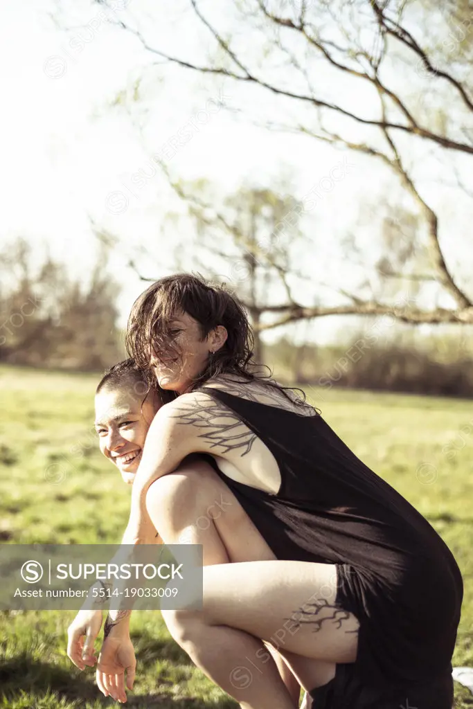 Piggyback of smiling female queer couple in grass meadow