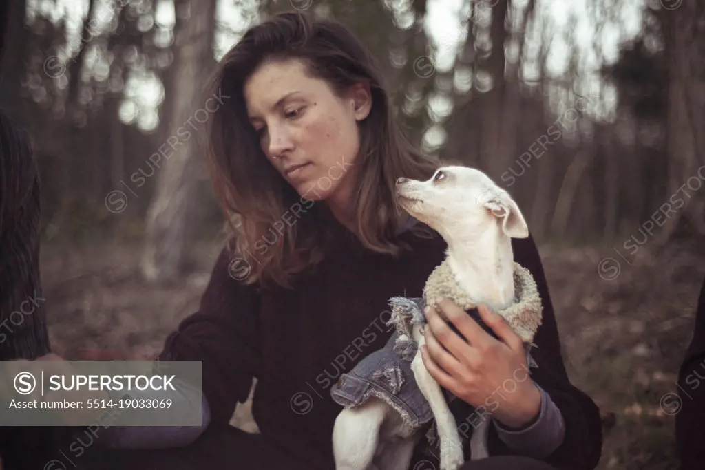 small white dog in jacket gazes at natural looking woman