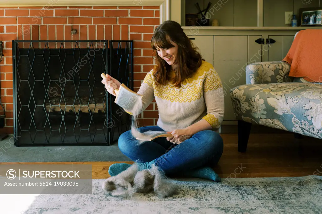 happy passionate millennial woman brushing wool roving by fireplace
