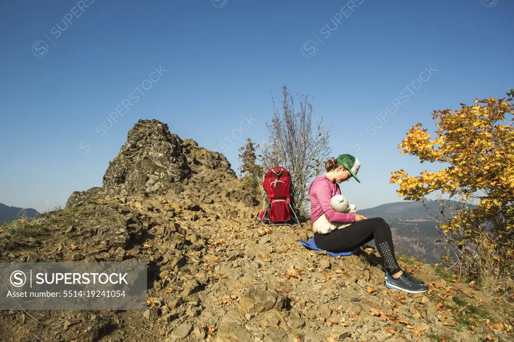 A young woman breast feeds an infant atop a mountain