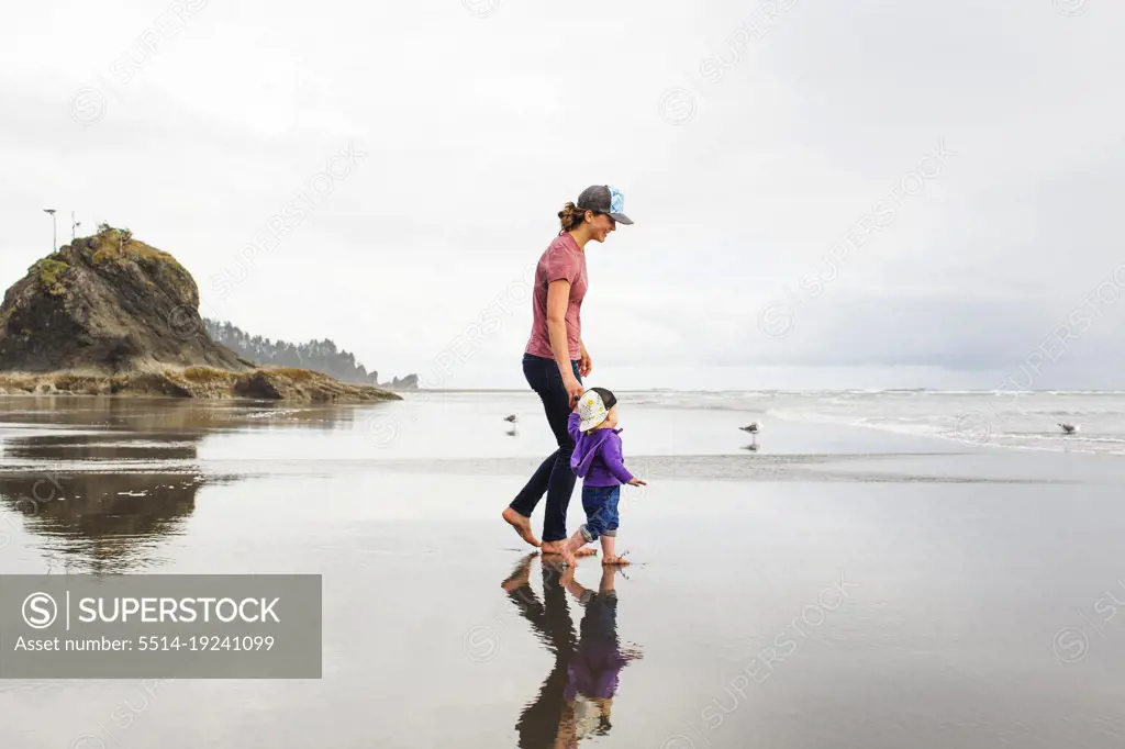 A young woman walks with a young child on a vast empty beach