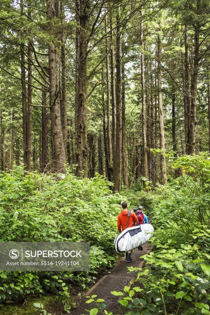 A man carrying a surfboard walks down a forested path