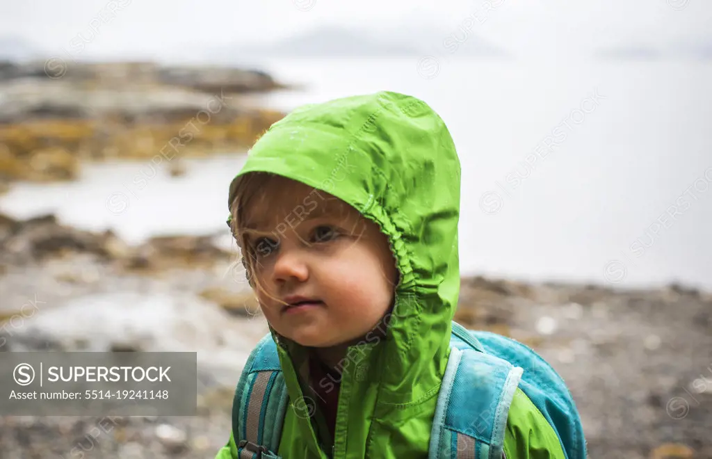 Young child in rain coat on rocky beach