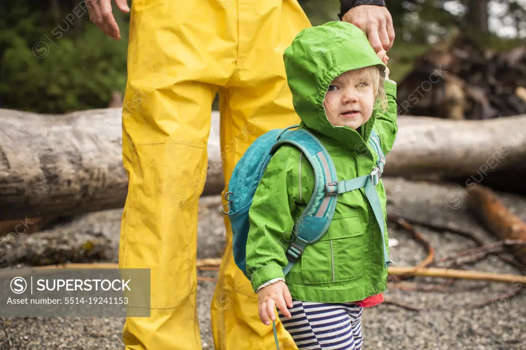 Young child in rain coat on rocky beach holding dad's hand